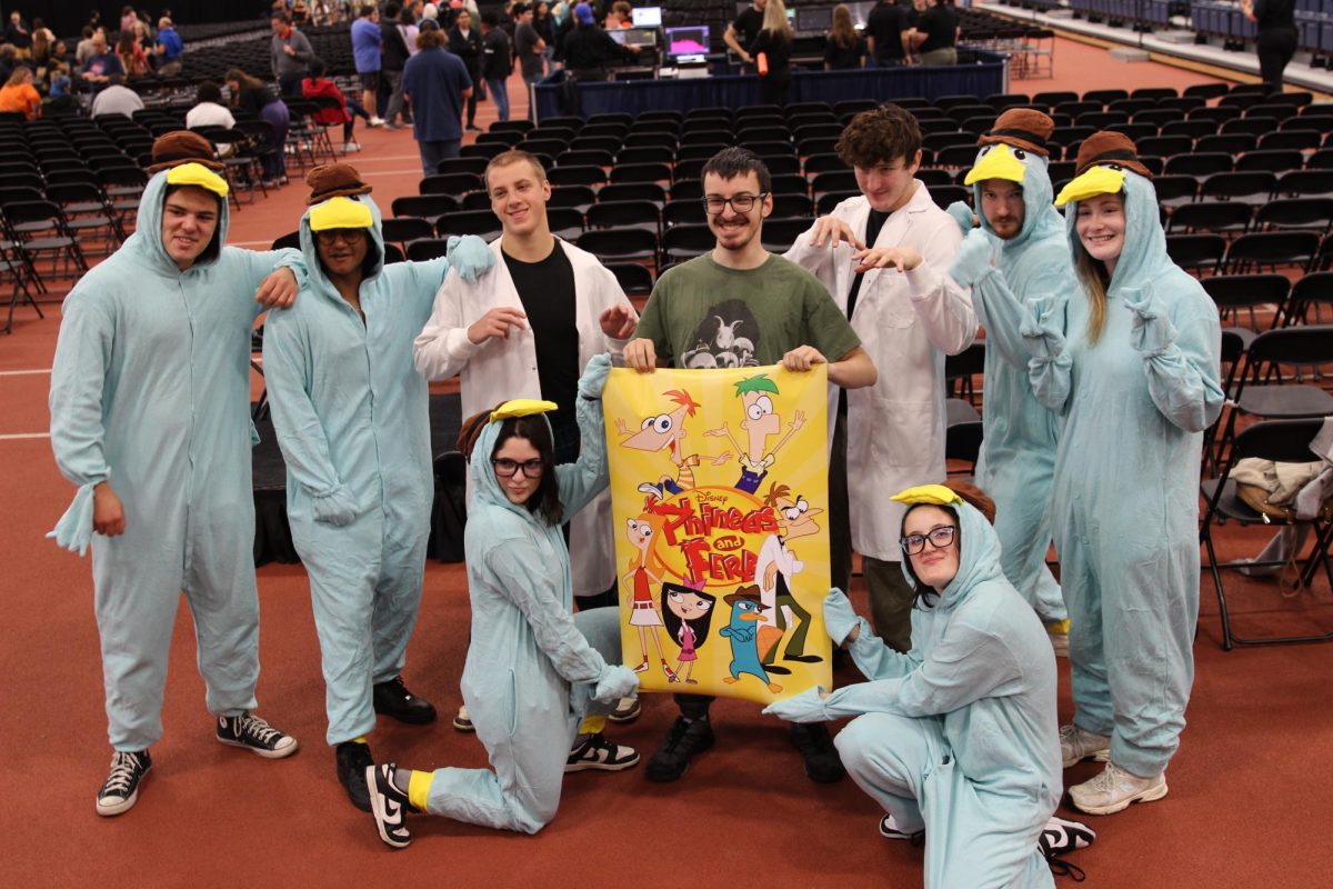 Attendees dressed as "Phineas and Ferb" characters pose beside a poster for the show after the conclusion of Dan Povenmire's speaker event at RIT in Henrietta, N.Y., on Oct. 18, 2025.